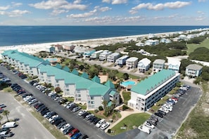 A coastal hotel with multiple buildings, a parking lot, and a beach in the background. - Pool view studio with onsite sauna, beach access, and pickleball courts (Gulf Shores)