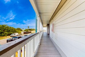 A covered porch with a wooden railing, a clear blue sky, and parked vehicles in the background. - Pool view studio with onsite sauna, beach access, and pickleball courts (Gulf Shores)
