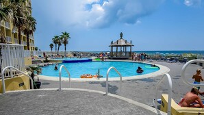 A pool area with a gazebo, palm trees, and a view of the ocean. - Dreamy beach condo with water views, balcony, pool & beach access (Orange Beach)