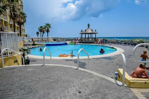 A pool area with a gazebo, palm trees, and a view of the ocean. - Dreamy beach condo with water views, balcony, pool & beach access (Orange Beach)