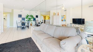 Ein modernes Wohnzimmer mit einer Couch, einem Esstisch, Stühlen, einem Fernseher und einem Deckenventilator.