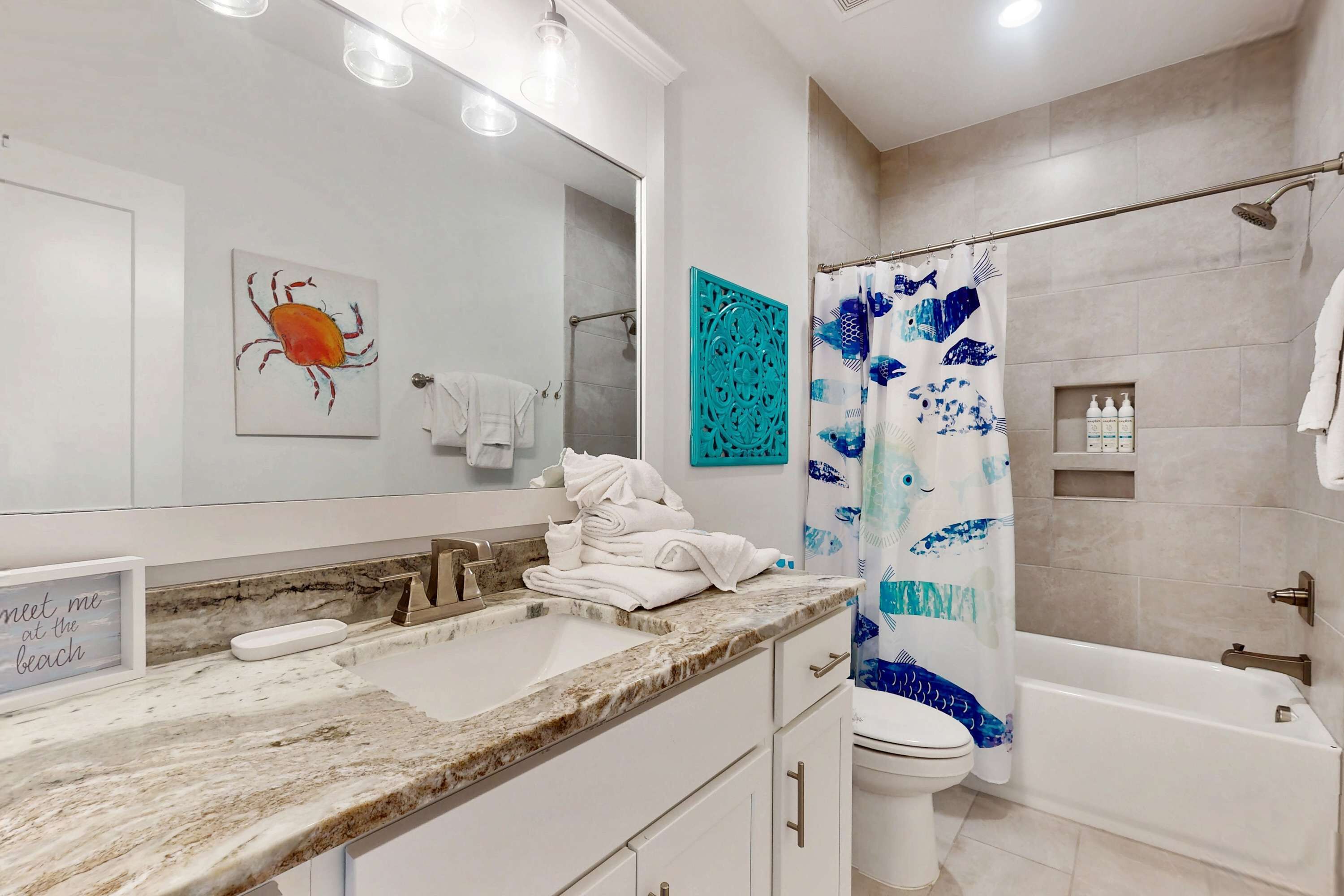 A bathroom with a marble sink, a bathtub, a shower curtain with a fish pattern, and a wall-mounted towel rack.