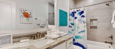A bathroom with a marble sink, a bathtub, a shower curtain with a fish pattern, and a wall-mounted towel rack.