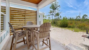 Eine überdachte Terrasse mit Holzmöbeln, Blick auf den Strand und ein Gebäude mit weißer Fassade.
