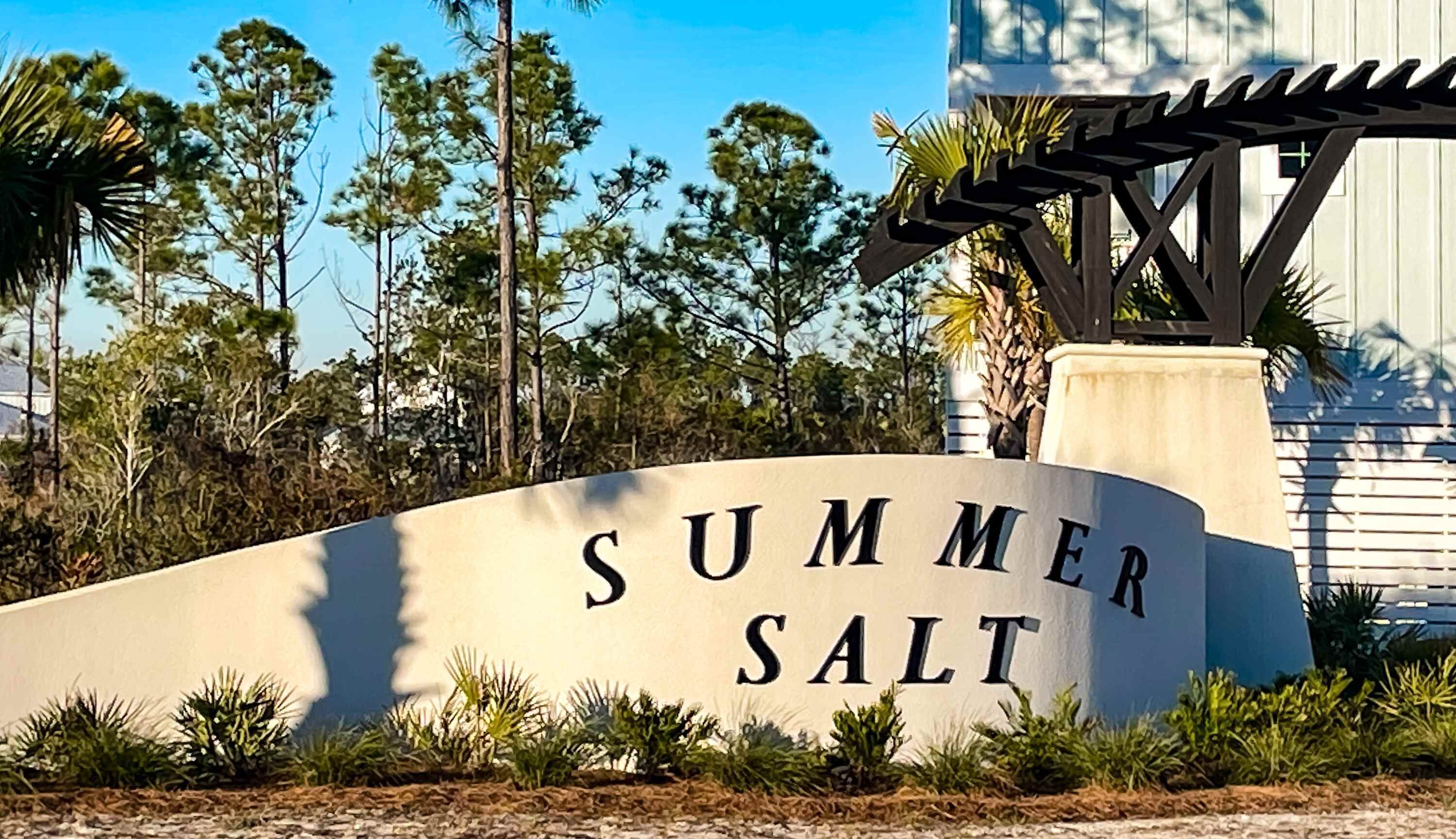 A sign with 'SUMMER SALT' written on it, surrounded by greenery and trees.