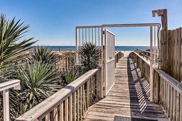 Ein Holzsteg führt zu einem Strand unter blauem Himmel.