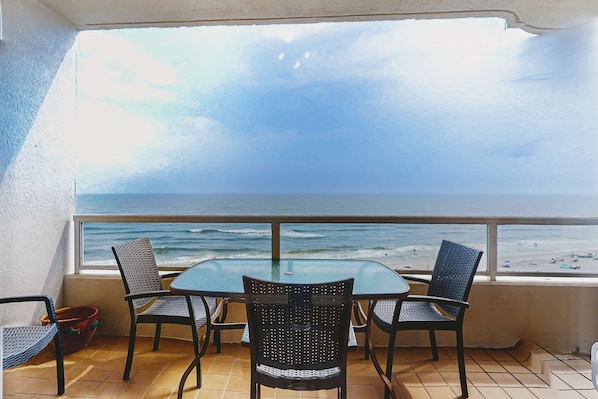 Varanda com mesa de vidro e quatro cadeiras, com vista para o oceano.