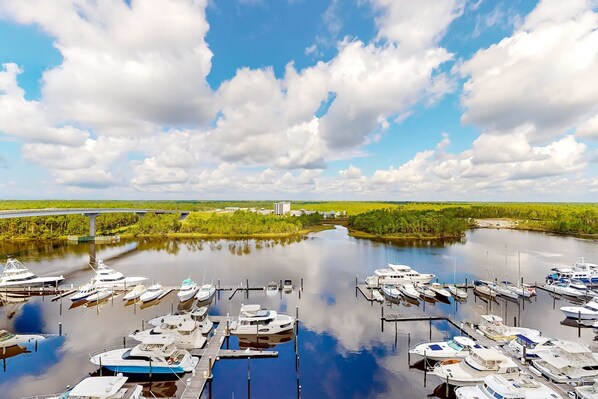 A marina with boats docked, a bridge in the background, and a river. - Clean & spacious Canalfront condo with pool & hot tub on-site, gorgeous sunsets (Orange Beach)