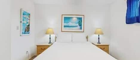A bedroom with a bed, two bedside tables with lamps, a ceiling fan, and a framed picture on the wall.