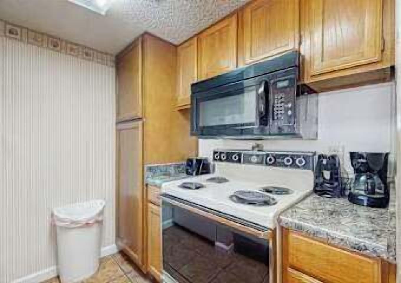 A compact kitchen with wooden cabinets, a microwave, an oven, and a coffee maker.