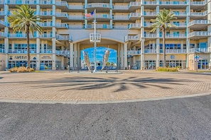 A multi-story hotel with a central entrance, palm trees, and a blue awning. - Amazing riverfront condo with pool, hot tub, balcony, & washer/dryer (Orange Beach)