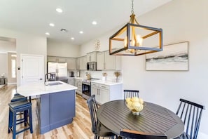 A modern kitchen with a central island, white cabinetry, and a dining area with a round table and chairs. - Surprise Getaway with Heated Pool Included! Close to Spring Training and Golf! (Surprise)