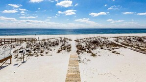 Ein Strand mit einer hölzernen Promenade, die zu einem Sandstrand führt, einem Holzzaun und einem wolkenlosen, blauen Himmel.