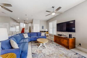 A living room with a blue sectional sofa, a round coffee table, a TV on a wooden stand, and ceiling fans.