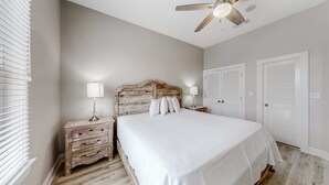 Ein Schlafzimmer mit einem hölzernen Kopfende, einem großen Bett, zwei Nachttischen mit Lampen und einem Deckenventilator.