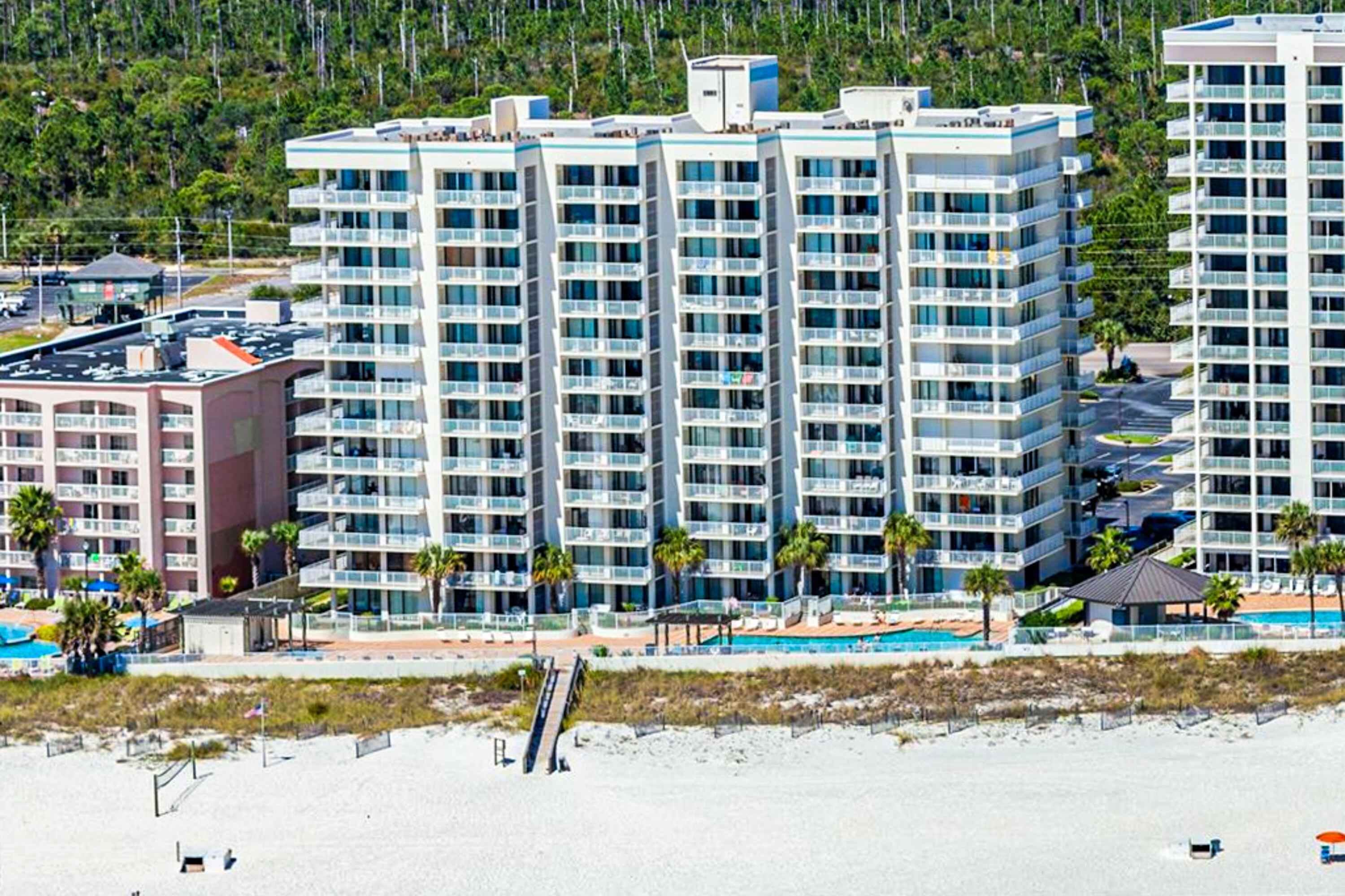 Et højt hotel med flere balkoner, en swimmingpool og udsigt til stranden.