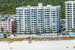 A high-rise hotel with multiple balconies, a swimming pool, and a beach view. - Fun, beachy condo in Gulf-front complex with pool & tennis court (Orange Beach)