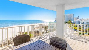 Ein Balkon mit Blick auf Strand und Meer, inklusive Tisch, zwei Stühlen und einer Geländer.