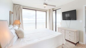 Ein Hotelzimmer mit Bett, Fernseher, Deckenventilator und Meerblick.