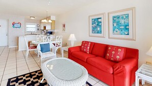 A living room with a red sofa, white chairs, a dining table, and a ceiling fan. - Gorgeous home in beachfront complex with pool, tennis court & WiFi (Orange Beach)