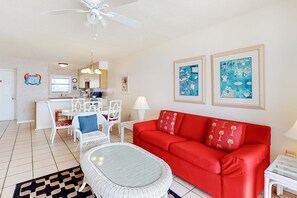 A living room with a red sofa, white chairs, a dining table, and a ceiling fan. - Gorgeous home in beachfront complex with pool, tennis court & WiFi (Orange Beach)