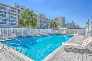 Piscina com deck de madeira, espreguiçadeiras brancas e cerca branca.