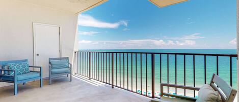 A balcony with a view of the ocean, a door, and two blue chairs.