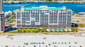 A large hotel with multiple floors, a swimming pool, and a beach area with umbrellas. - Gulf-front condo with shaded balcony, pools, hot tubs, gym & beach access (Orange Beach)