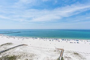 Ein Strand mit sandigem Ufer, einer Holzpromenade und einem klaren, blauen Himmel.