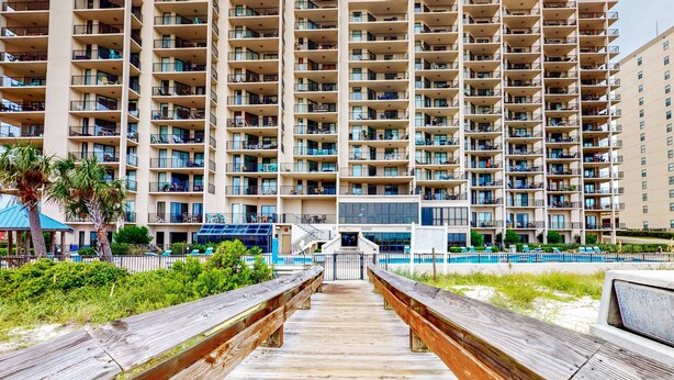 Un hôtel à plusieurs étages doté de balcons, d’un espace piscine et d’une promenade en bois menant à l’entrée.