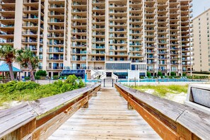 A multi-story hotel with balconies, a pool area, and a wooden boardwalk leading to the entrance. - Renovated, Gulf-front condo with great beach view, pools, hot tubs, & tennis (Orange Beach)