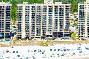 A high-rise hotel with multiple balconies, a pool area, and a beach with umbrellas. - Beachfront condo with Gulf views, balcony, pool, hot tub, sauna & gym (Orange Beach)