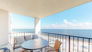 Ein Balkon mit rundem Tisch und Stühlen, Blick auf den Strand und einer Geländer.