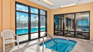 An indoor swimming pool with clear windows, a white chair, and a view of the outside. - Gulf-front condo with inviting balcony, amazing views, pool & hot tub (Orange Beach)