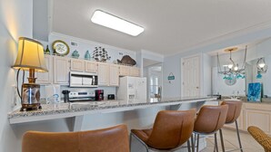 A kitchen with a central island, bar stools, a lamp, and decorative items. - Gulf-front condo with inviting balcony, amazing views, pool & hot tub (Orange Beach)
