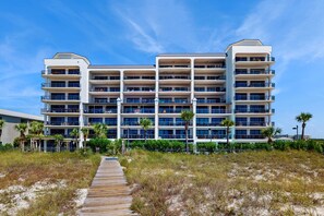A multi-story hotel with balconies, a wooden boardwalk, and a clear sky. - 4th-floor Gulf-front condo with balcony, pool, hot tub, sauna & gym (Orange Beach)