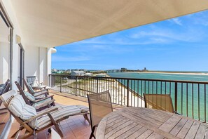 A balcony with a view of the ocean and a bridge, furnished with striped chairs and a table. - 4th-floor Gulf-front condo with balcony, pool, hot tub, sauna & gym (Orange Beach)