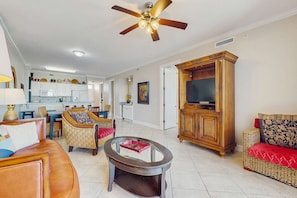 A living room with a sofa, armchair, coffee table, wooden cabinet, and a ceiling fan. - 4th-floor Gulf-front condo with balcony, pool, hot tub, sauna & gym (Orange Beach)