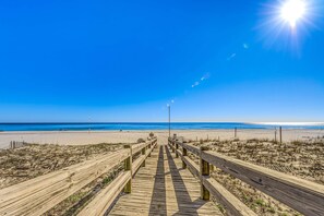 Une promenade en bois menant à une plage, avec un ciel dégagé.