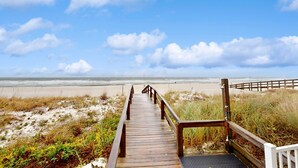 Un paseo marítimo de madera que lleva a una playa con cielo despejado.