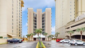 Un hotel de varios pisos con entrada central, estacionamiento y palmeras.