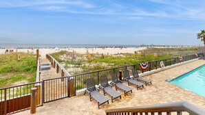 Zona junto a la piscina con sillones de descanso, una terraza de madera y vista a la playa y al océano.