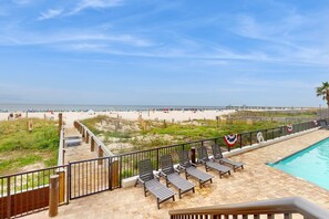 Ein Poolbereich mit Liegestühlen, einer Holzterrasse und Blick auf Strand und Meer.