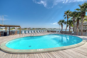 A swimming pool with a wooden deck, a covered seating area, and a view of a body of water. - Gulf front condo with great views, shared pools & beach access (Orange Beach)