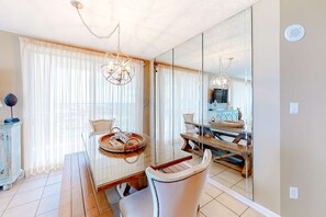 A dining area with a glass table, chairs, and a chandelier. - Large beachfront condo with views from private balcony and shared hot tub & pool (Orange Beach)