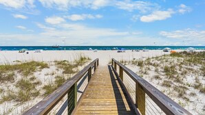 Une promenade en bois menant à une plage où l’on trouve des parasols et des chaises de plage.