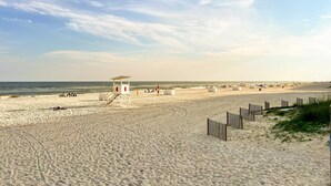 A sandy beach with a lifeguard tower, ocean view, and beach umbrellas. - Brilliant beach house located walking distance to beach with community pool (Orange Beach)