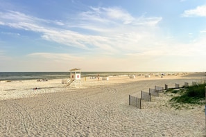 Ein Sandstrand mit einem Rettungsturm, Blick auf den Ozean und Strandstühlen.