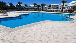 A swimming pool with lounge chairs, a tiled deck, and a row of houses in the background. - Brilliant beach house located walking distance to beach with community pool (Orange Beach)