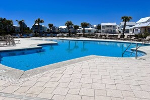 Ein Schwimmbecken mit Liegestühlen, einer gefliesten Terrasse und einer Reihe von Häusern im Hintergrund.